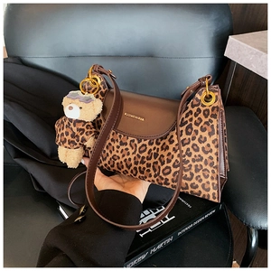 Détail du sac à bandoulière léopard avec charm ours en peluche sur un livre de design