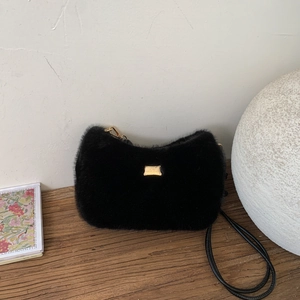 Sac à bandoulière chic en peluche noire avec logo doré sur une surface en bois