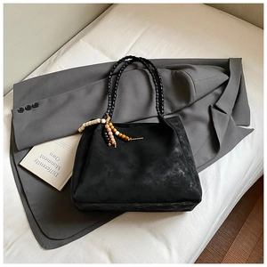 Detail of black suede tote bag with woven handles and bohemian tassel charm