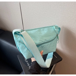 Detail of mint green nylon crossbody bag with zipper pockets and wide fabric strap