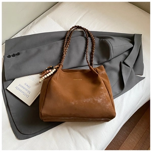 Detail of a brown suede tote bag with woven handles on a gray suit jacket