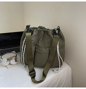 Detail of army green nylon messenger bag with drawstring and utility pockets on a desk