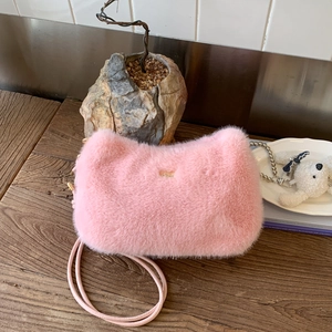 Détail du sac à main en peluche rose avec plaque logo dorée et fine bandoulière longue