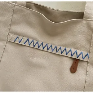Close-up of beige canvas tote bag with blue wavy embroidery and minimalist outer pocket