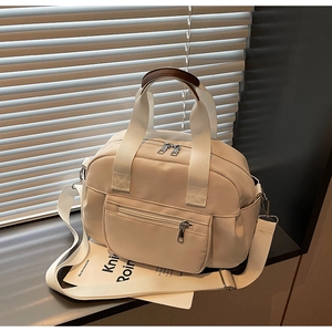Close-up of off-white nylon tote bag showing front zipper pocket and brown leather handles