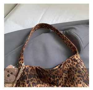 Detail of leopard print tote bag featuring a plush dog charm and wide comfort handle