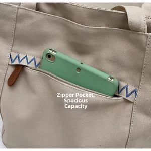 Detail of exterior zipper pocket on canvas tote bag showing storage for a mobile phone