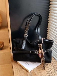 Vintage black faux suede tote bag with leather straps and decorative tassel on a wooden desk