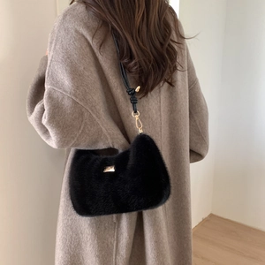 Détail du sac bandoulière en fausse fourrure noire avec logo doré sur manteau d'automne