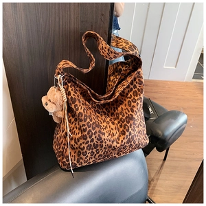 Detail of leopard print tote bag with brown plush bear charm on a dark chair