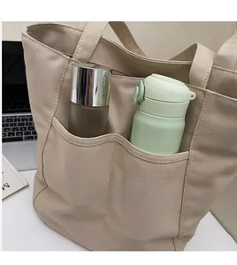 Detail view of large beige canvas tote bag with front pockets in a workspace setting