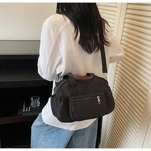Detail of black nylon tote bag with reinforced handles and multiple zip pockets shown in use