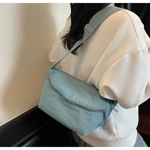 Close-up of light blue nylon crossbody bag featuring front zipper pocket and strap detail
