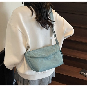 Detail view of light blue nylon crossbody bag with adjustable strap and front zipper pocket
