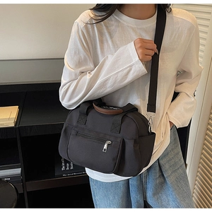 Detail of black canvas tote bag with brown leather handles and wide fabric strap on model