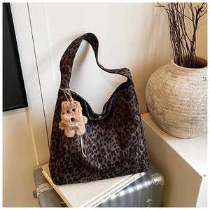 Detailed view of leopard print tote bag with brown plush puppy charm on a vintage suitcase