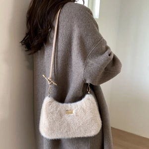 Gros plan du sac bandoulière en peluche crème avec plaque logo dorée élégante