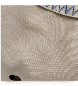 Detail of beige canvas fabric with blue wavy stitching and a small brown bear embroidery
