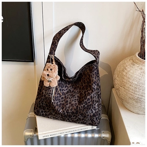Detail of leopard print tote bag with plush bear charm on a silver suitcase