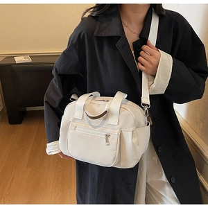 Detail of white nylon shoulder bag with wide strap and metallic zip pockets on model