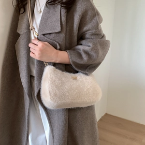 Détail d'un sac bandoulière en fausse fourrure beige avec logo doré sur manteau gris