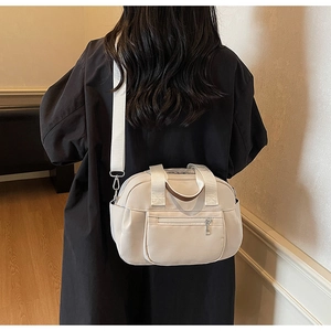 Detail of a minimalist off-white canvas tote bag with adjustable strap and brown leather handle