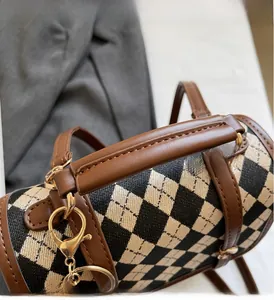Close-up of retro checkered barrel bag showing stitched leather handles and gold hardware