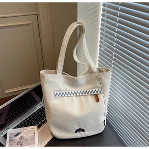 Detail of cream canvas tote bag featuring blue zigzag stitching and dog embroidery