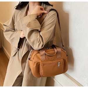 Brown nylon tote bag with wide shoulder strap shown on model in a stylish trench coat