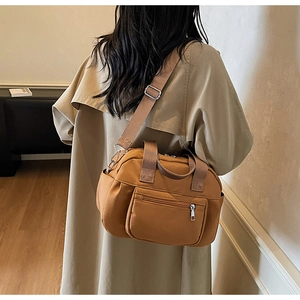 Lifestyle view of a camel nylon tote bag worn as a crossbody with a beige trench coat