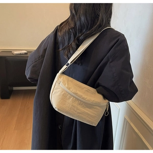 Nylon dumpling crossbody bag in light khaki shown on a model with a black long coat
