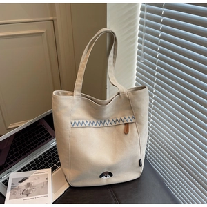 Close-up of beige canvas tote bag featuring blue wave embroidery and a cute puppy detail