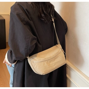Detail of a minimalist beige crossbody bag showing its crescent shape and adjustable strap