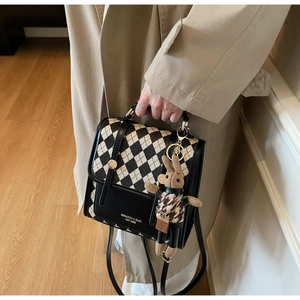 Detail of checkered crossbody bag with cute rabbit charm held by model in trench coat