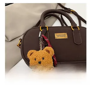 Close-up of a brown teddy bear charm with woven cord on a matte leather handbag