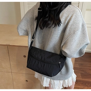 Rear view of a model wearing a black nylon crossbody bag with adjustable strap and silver zipper