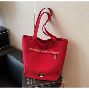 Detail of red canvas tote bag with cartoon embroidery and zigzag stitching on books
