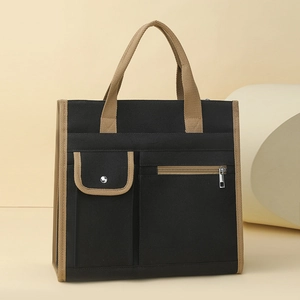 Detail of canvas tote bag showing black fabric with khaki handles and front zipper pocket