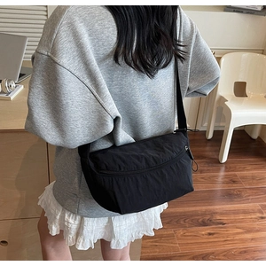 Detail of minimalist black nylon crossbody bag with front zipper and wide strap
