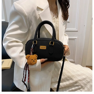 Detail of black bowling bag with golden metal plaque and brown plush bear charm