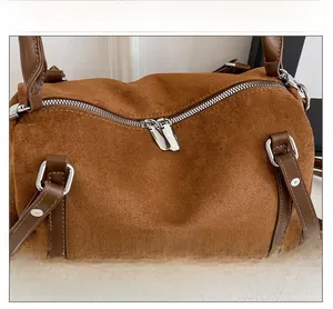 Detail of a brown suede Boston bag featuring double zippers and leather handles