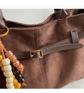 Close-up of brown suede shoulder bag featuring leather straps and beaded wood charms