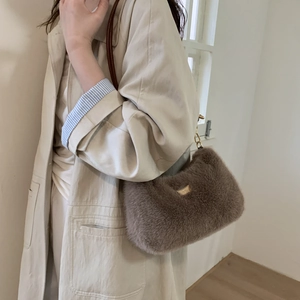 Détail du sac bandoulière marron en peluche avec logo doré sur tenue de trench élégante