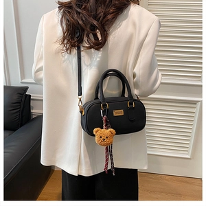 Detail of black Boston bag featuring a plush bear pendant and gold metal logo plate