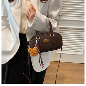 Detailed shot of a brown Boston style bag with teddy bear charm and striped ribbon décor