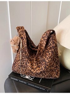 Large leopard print tote bag with plush bear charm on a minimalist bookshelf display