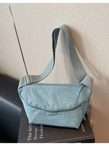 Minimalist light blue nylon crossbody bag with adjustable wide strap on textured background