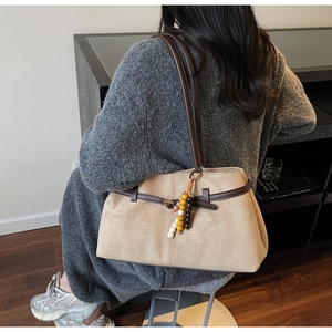 Detail view of beige suede tote bag with brown leather straps and wooden bead tassels