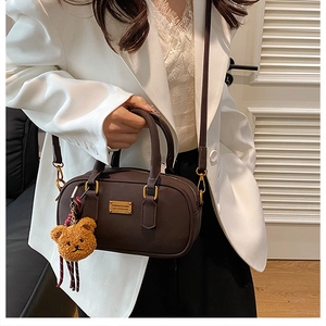 Detail of dark brown leather bowling bag with gold hardware and plush bear charm