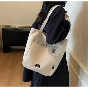 Detail of minimalist cream canvas tote bag with dog embroidery and blue wavy stitching